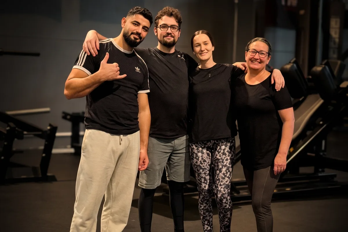Fyra glada deltagare står arm i arm på gymmet efter ett grupp-pass